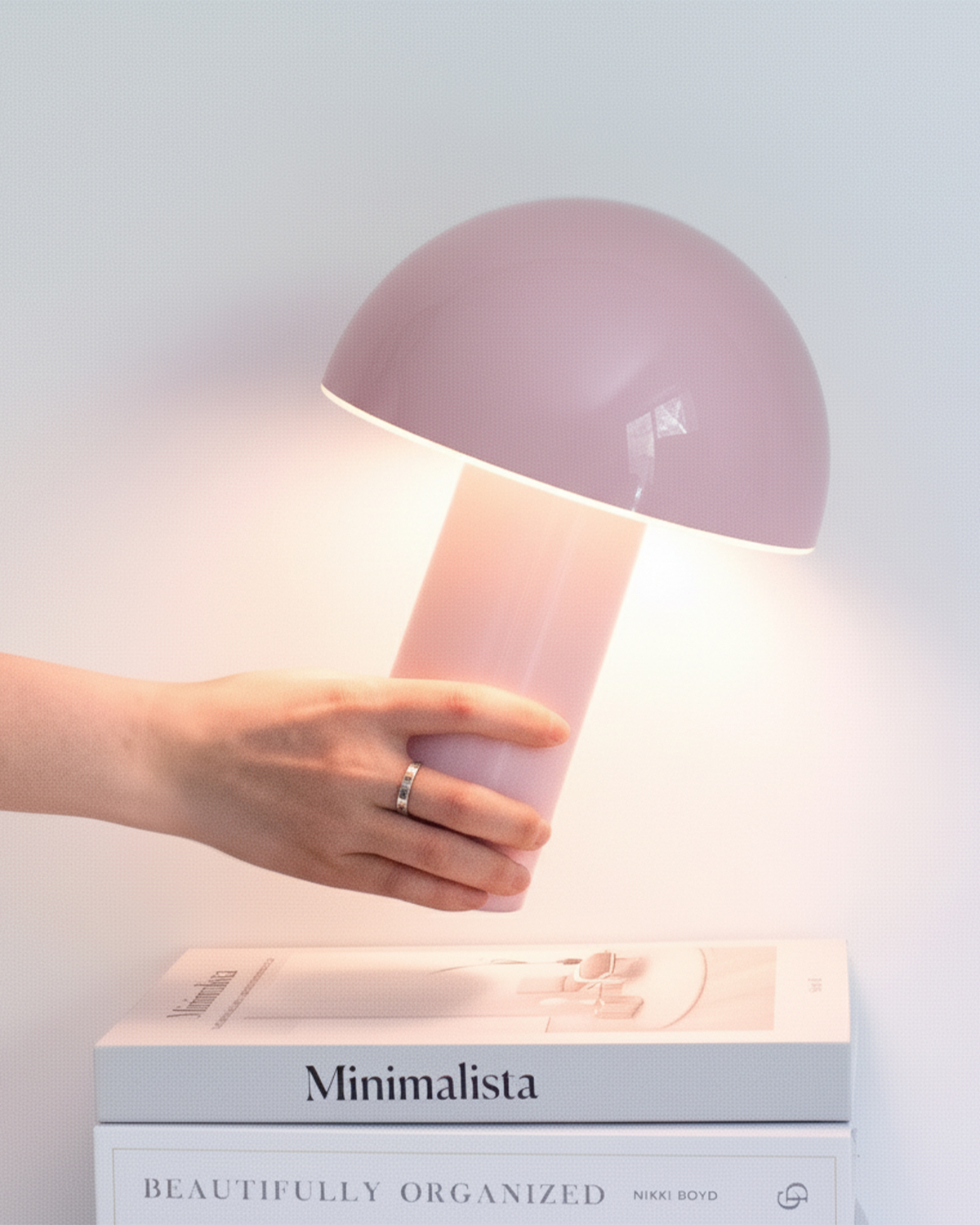 Pink table lamp being held by a hand on top of a 'Minimalista' book