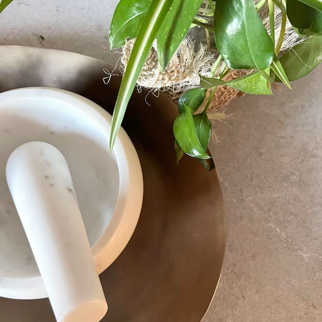 White mortar and pestle on a stone surface with green leaves in the background