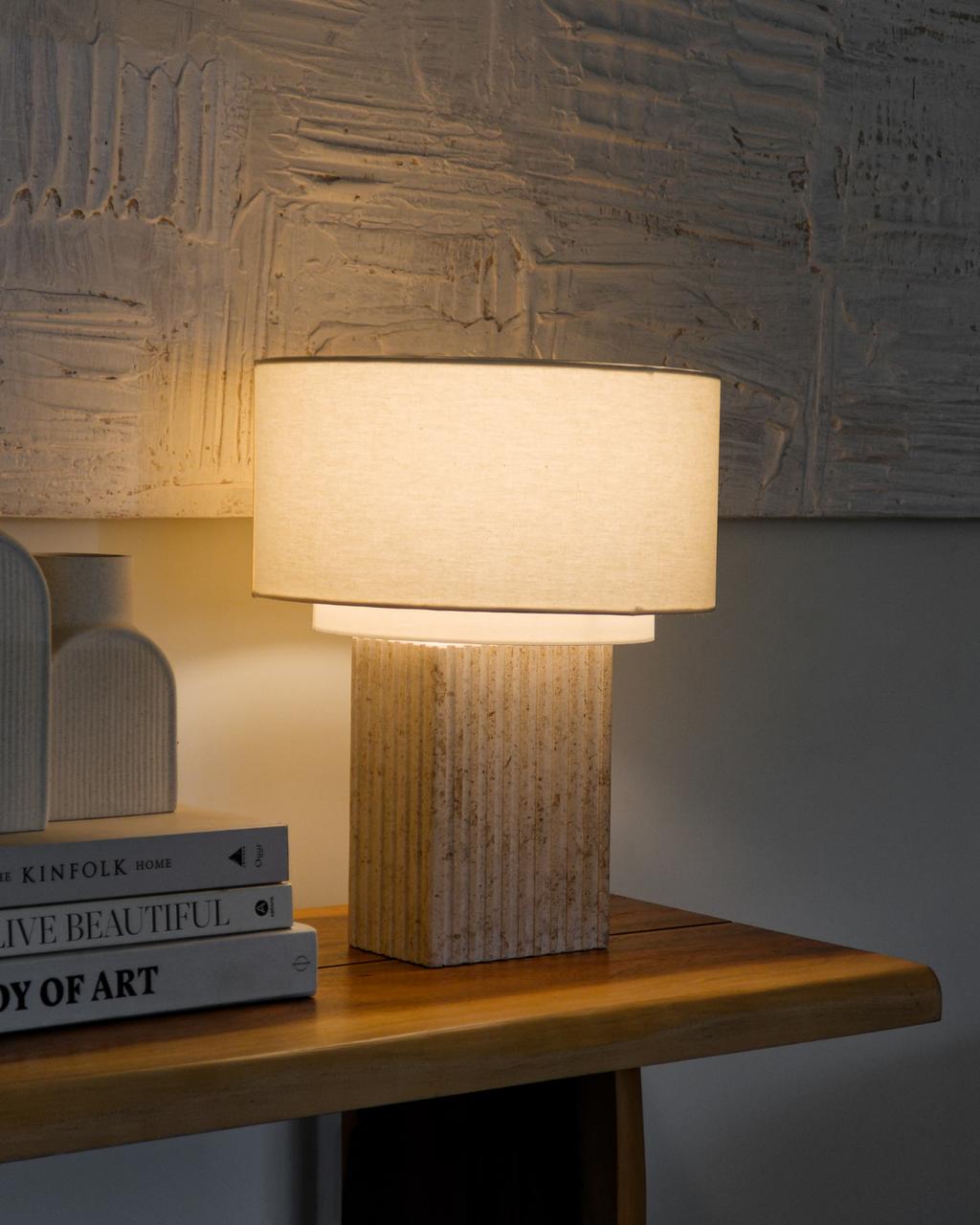 Table lamp with textured base on a wooden surface next to books, against a textured wall.