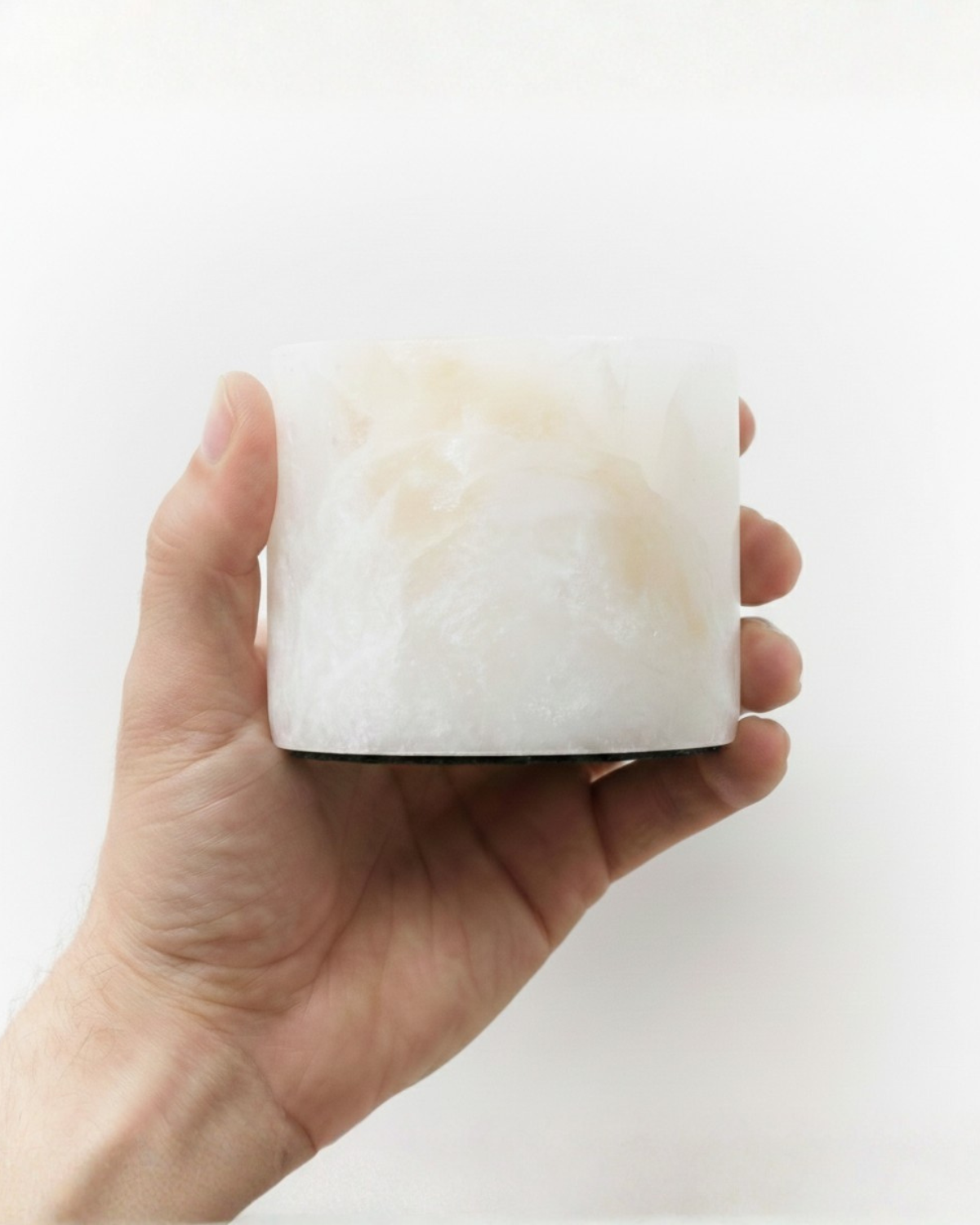 Hand holding a white marble-like cylindrical object against a white background
