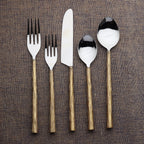 Set of silver cutlery with golden grooved handles on a brown textured background