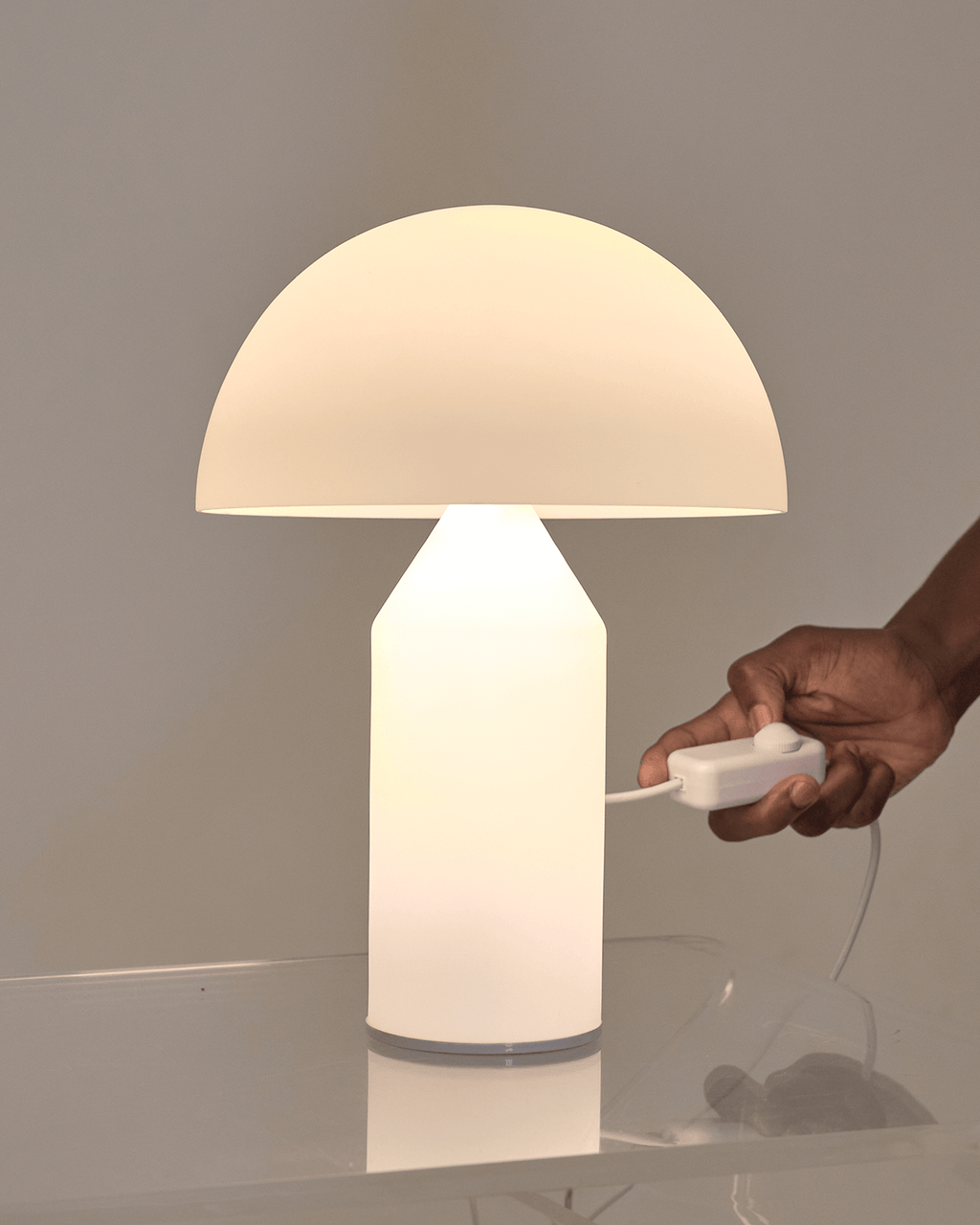Hand holding a white lamp with a beige shade on a reflective surface.