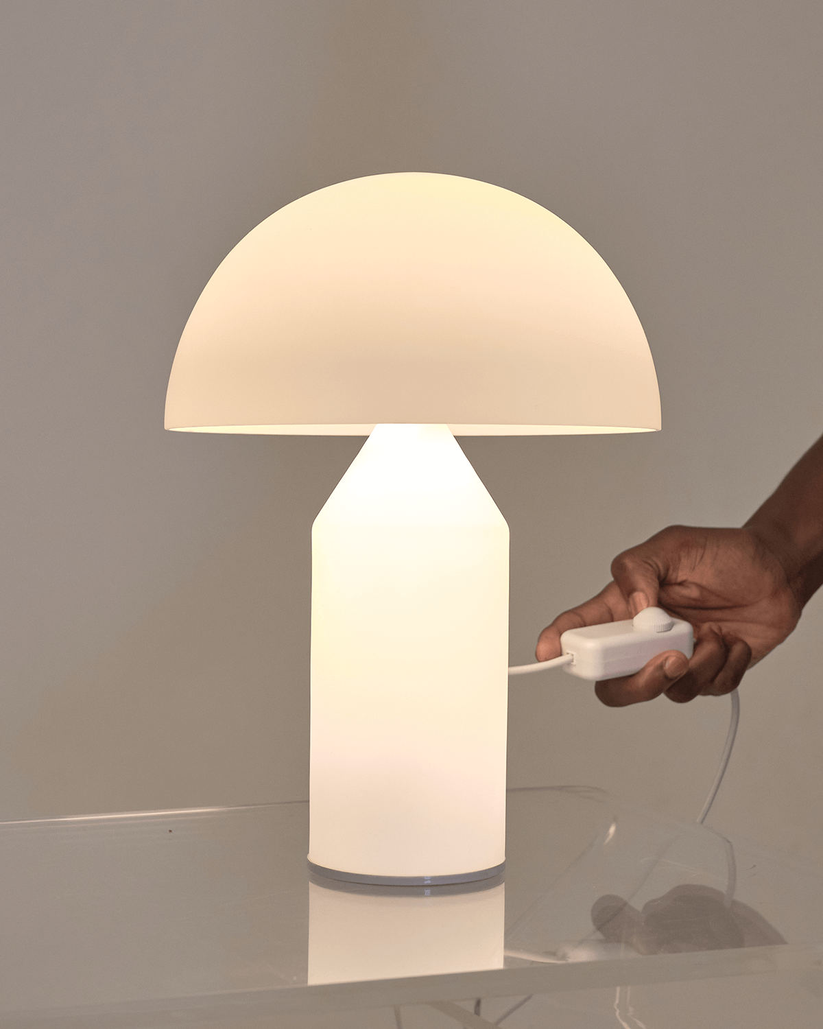 Hand holding a white lamp with a beige shade on a reflective surface.