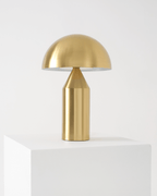 Gold table lamp on a white pedestal against a light gray background