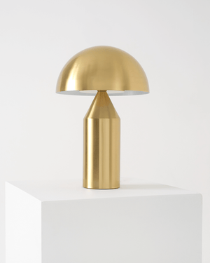 Gold table lamp on a white pedestal against a light gray background