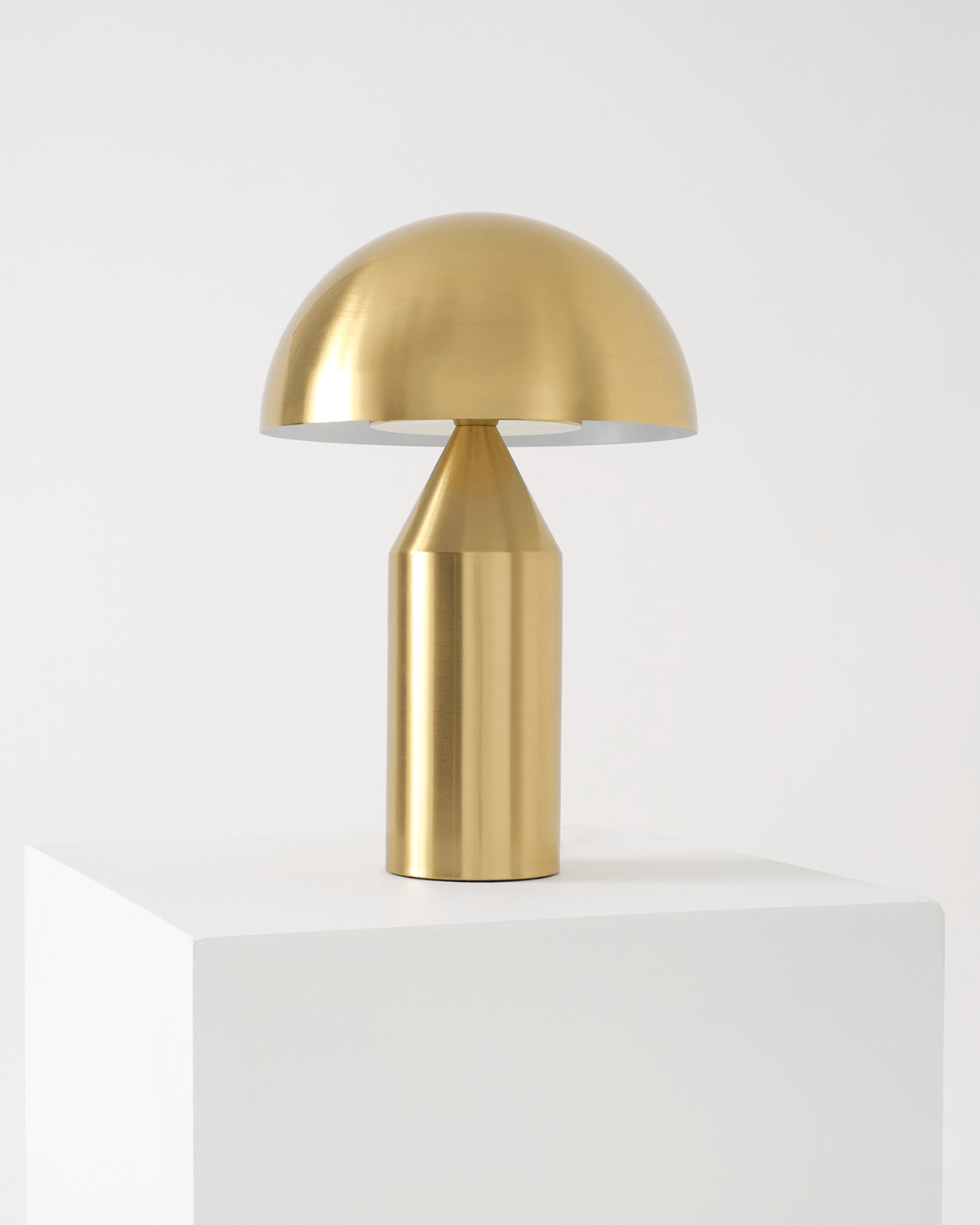 Gold table lamp on a white pedestal against a light gray background