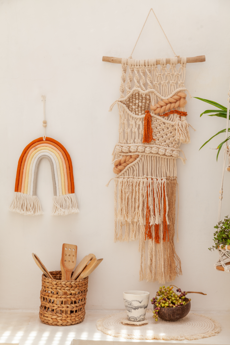 Macrame wall hanging and rainbow decoration on a white wall with a plant and basket.