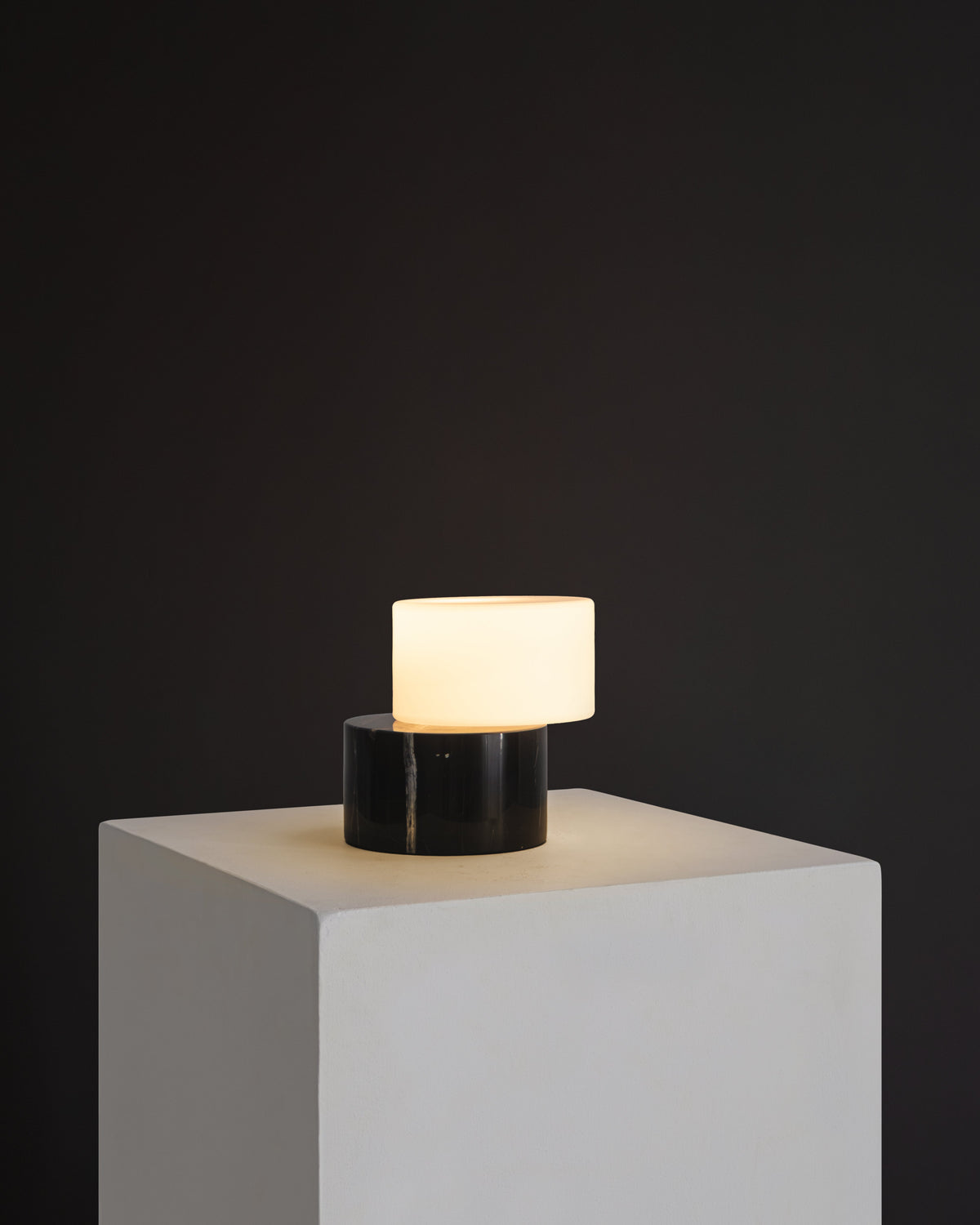 Modern table lamp with a black base and white shade on a gray pedestal against a dark background