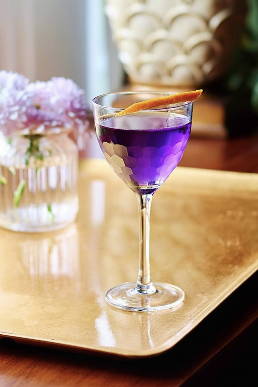 Purple cocktail with an orange twist on a gold table