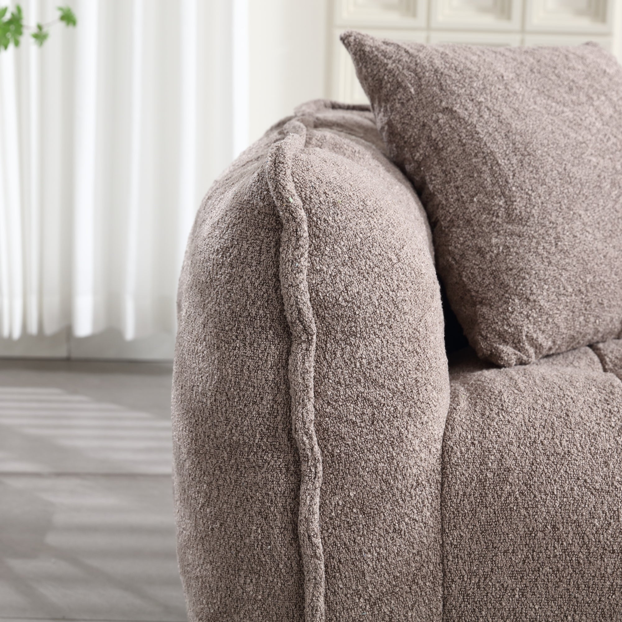 Close-up of a textured brown sofa with a pillow in a room with light-colored curtains.