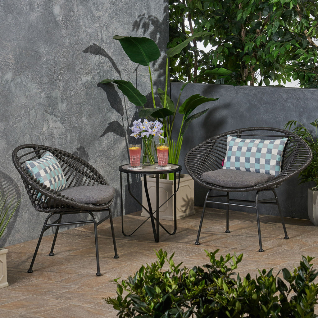 Outdoor patio set with two chairs, a small table, and decorative pillows on a patio with plants and a stone wall.