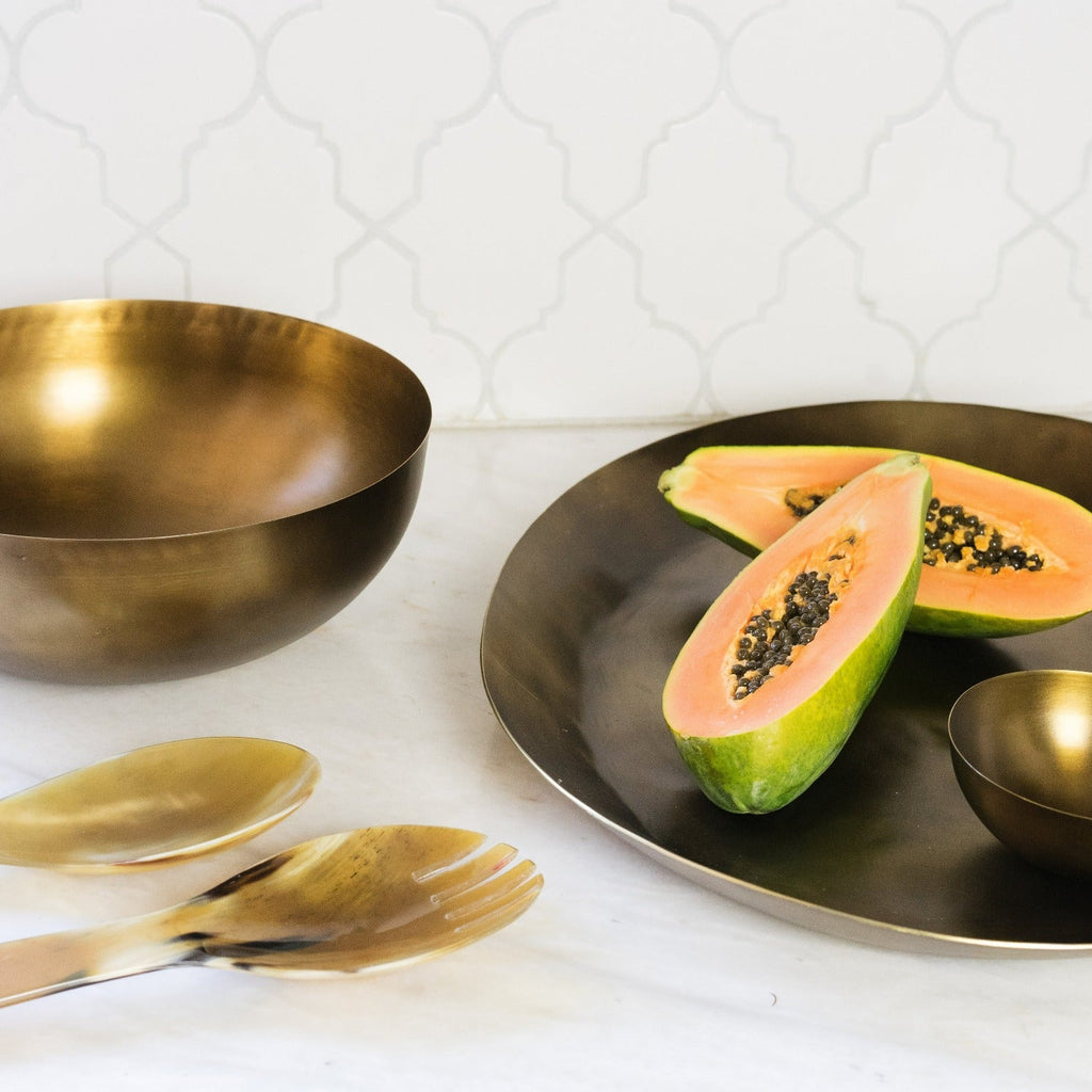 Gold bowls and spoons on a white surface with a halved papaya.