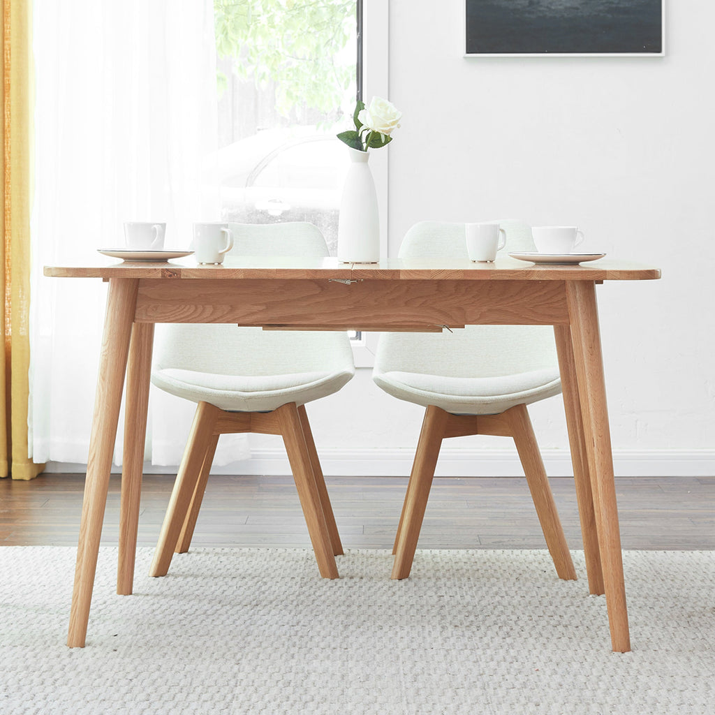 Wooden dining table with four white chairs in a bright room.