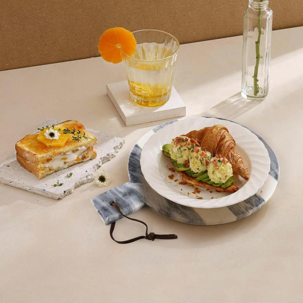 Breakfast setting with a croissant, toast, and glass of juice on a marble tray.