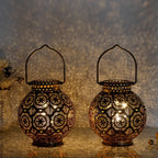 Two ornate metal lanterns with intricate designs on a reflective surface.