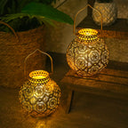 Two illuminated decorative lanterns on a wooden surface with a plant in the background.