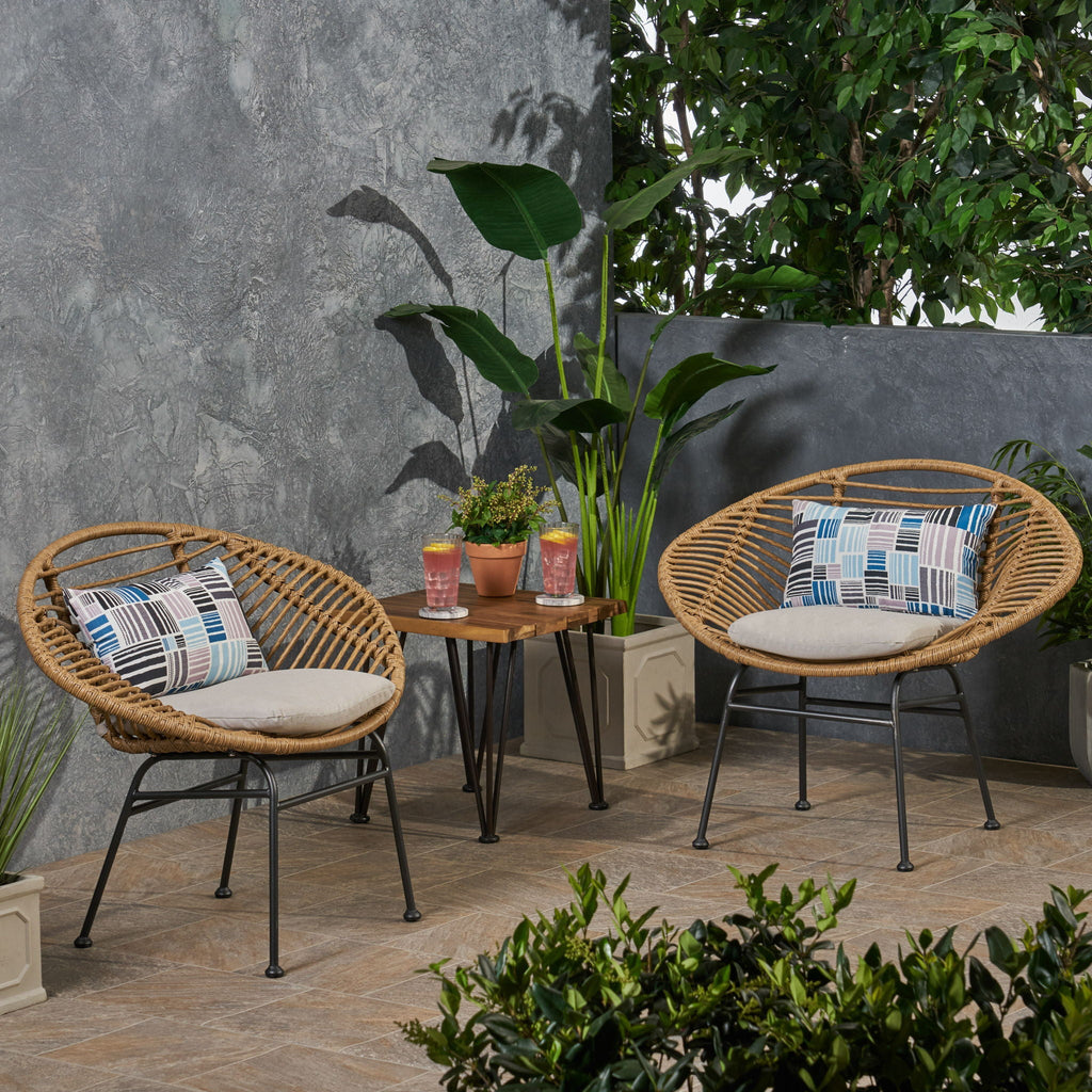 Outdoor patio set with two wicker chairs, a small table, and decorative pillows against a gray wall.