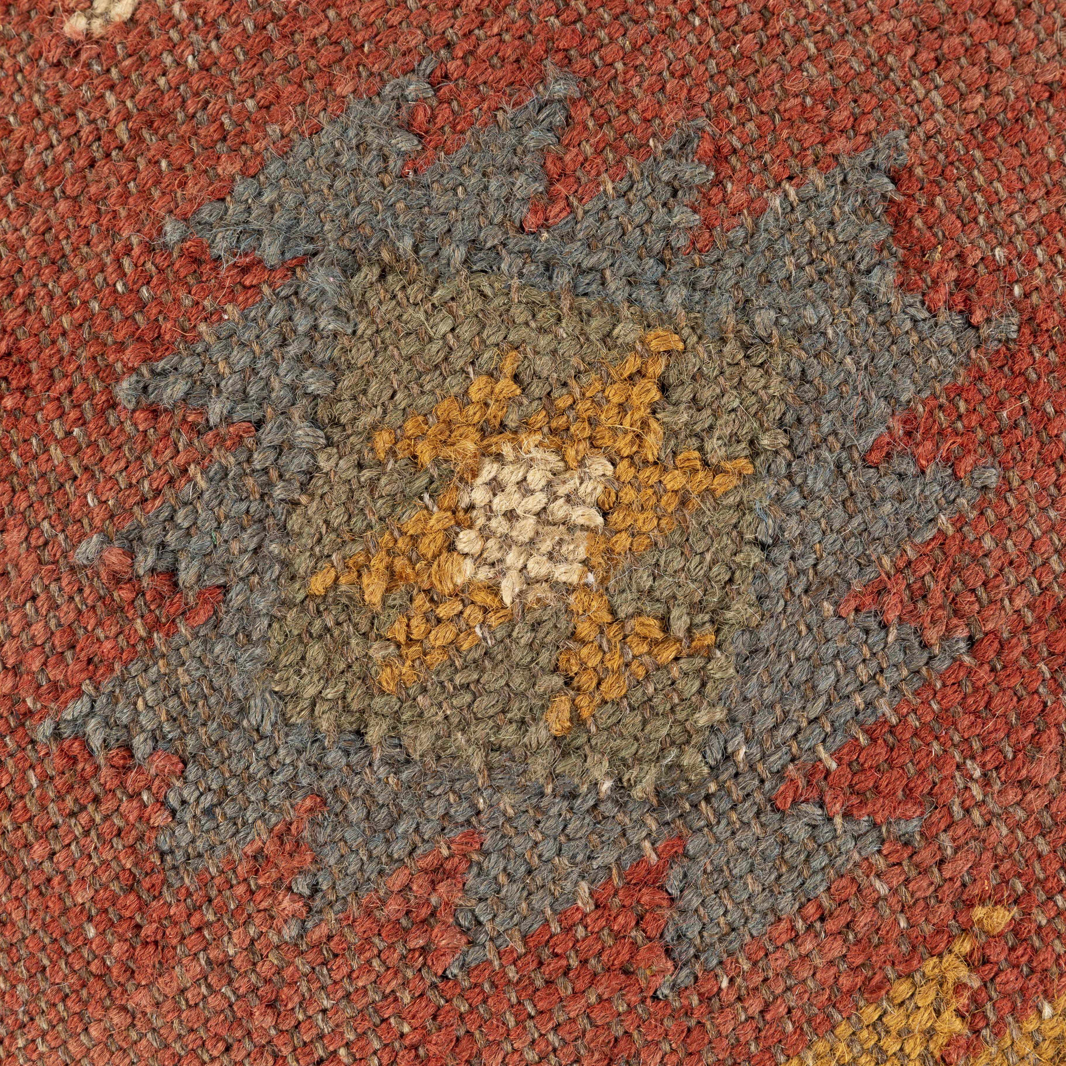Close-up of a textured pouf with a star-like pattern in red, brown, and beige.