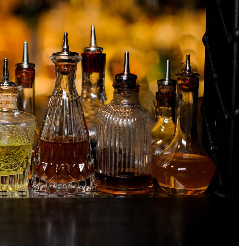 Set of glass bottles with liquid and metal nozzles on a reflective surface.