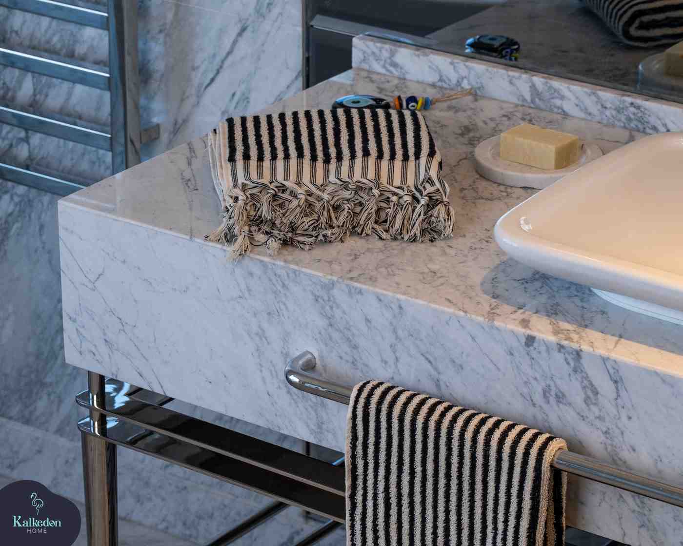 Black striped hand towel with fringe on a marble bathroom countertop near soap