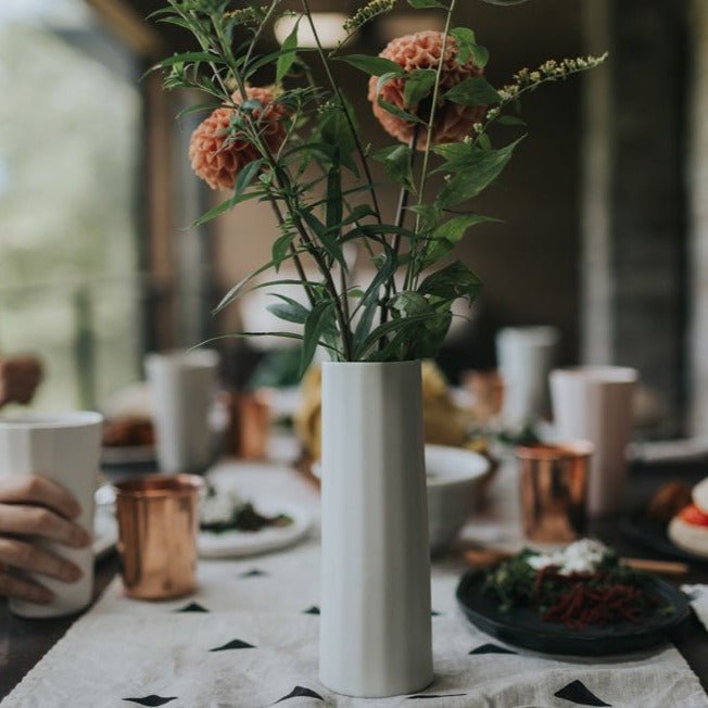 White vase with flowers on a table setting with plates and cups.