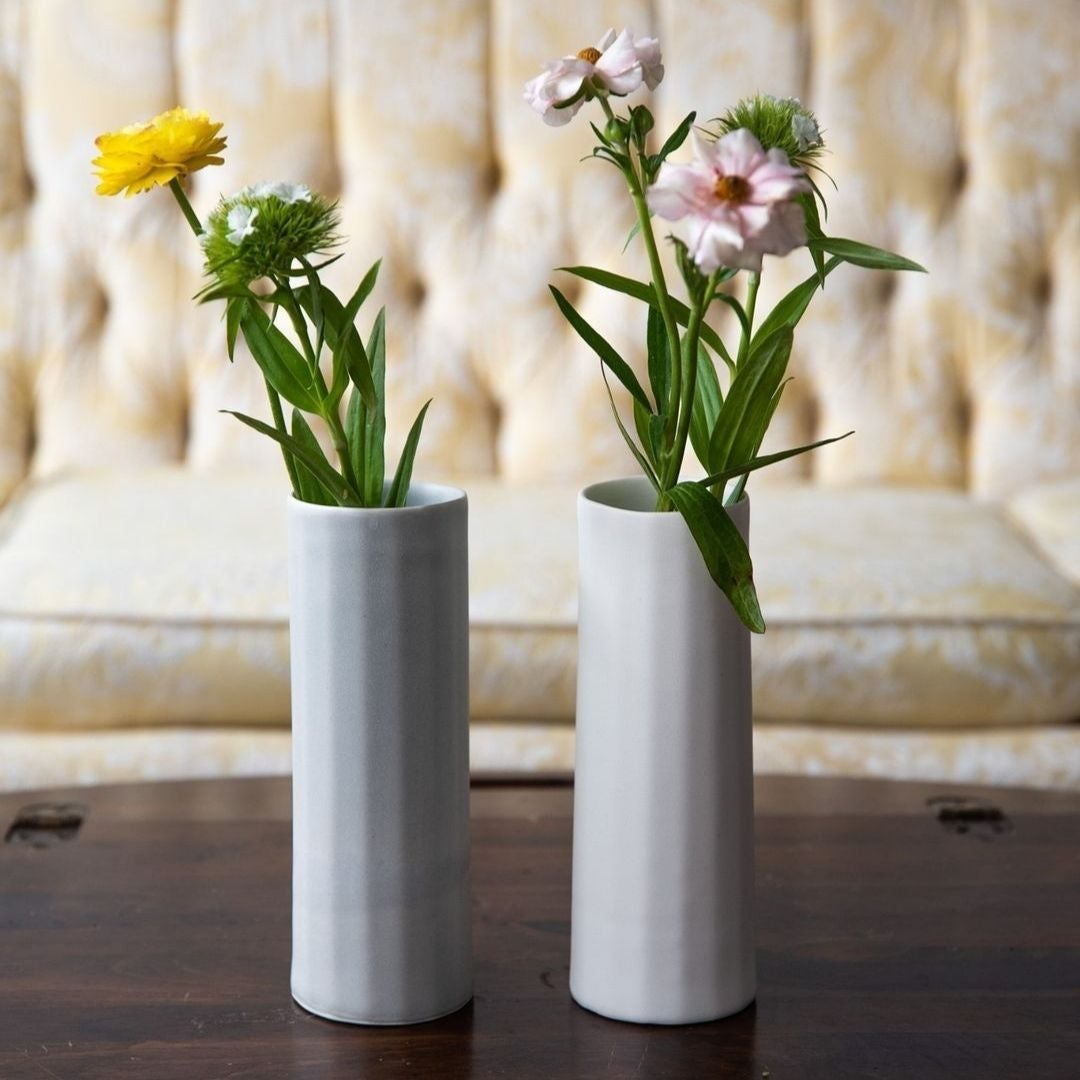 Two white vases with flowers on a wooden surface with a blurred background