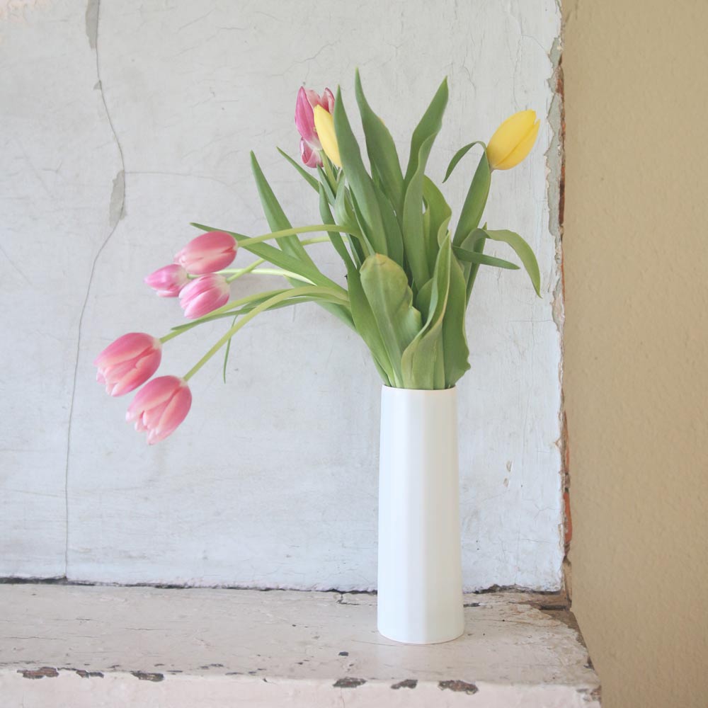 White vase with pink and yellow tulips against a textured wall.