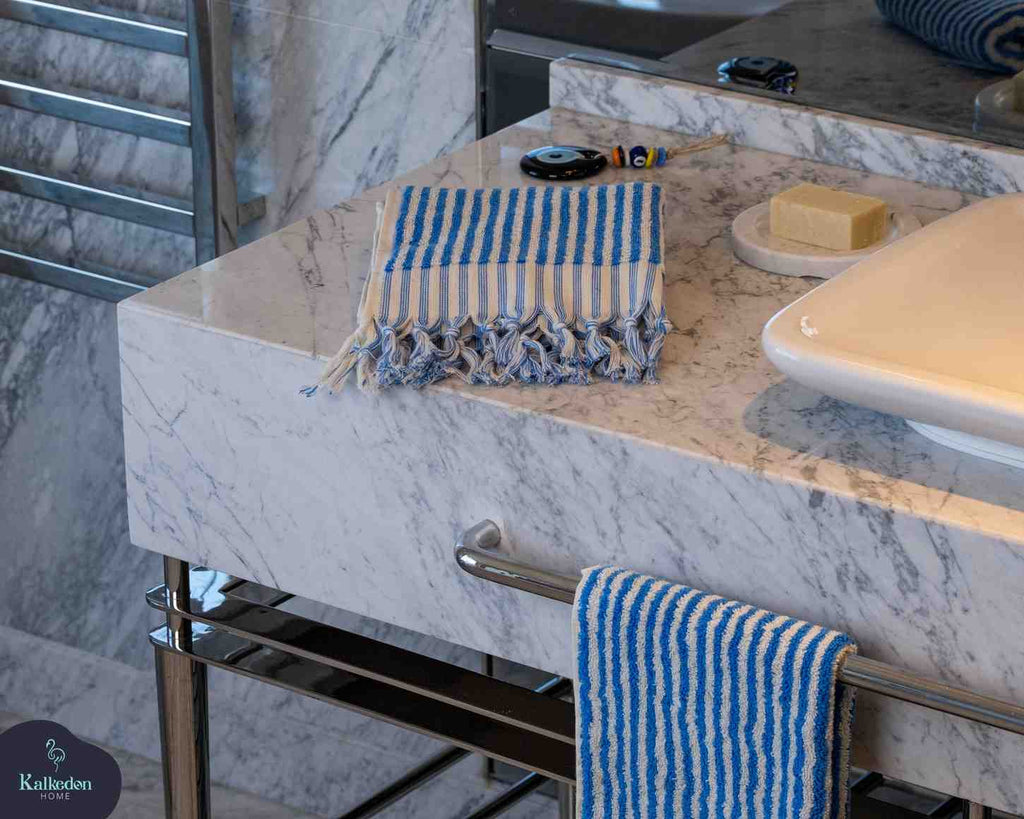 Blue and white striped hand towel with fringe on marble bathroom counter next to soap