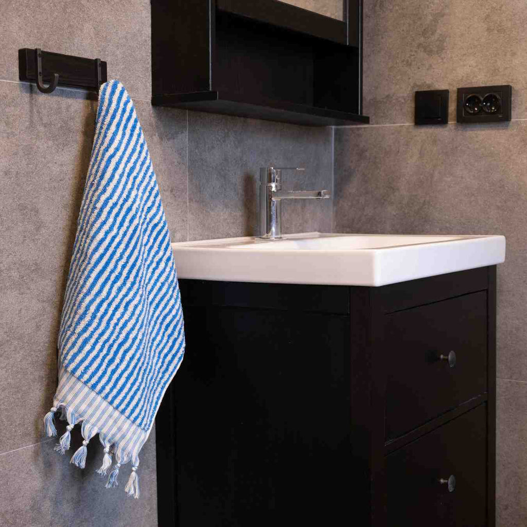 Blue striped hand towel with tassels hanging beside a modern bathroom sink