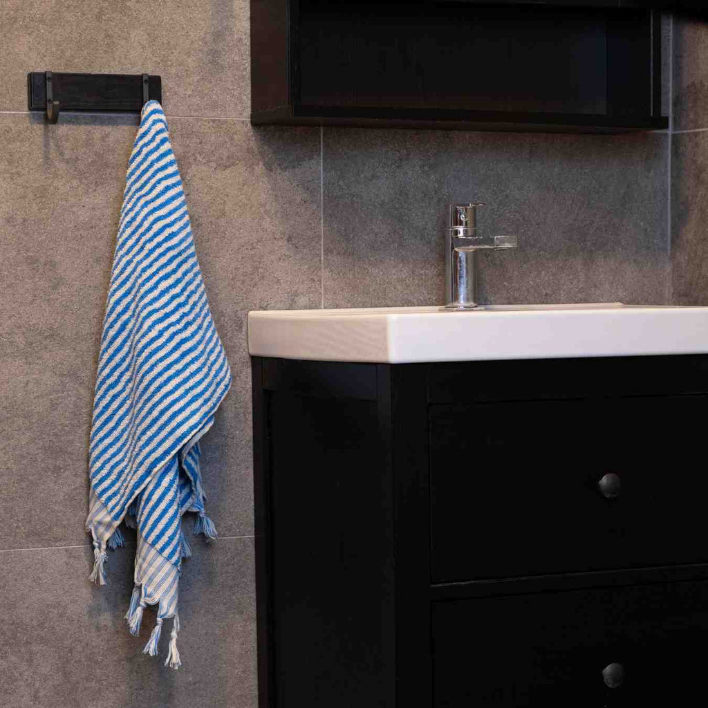 Blue striped hand towel hanging in modern bathroom beside black vanity sink.