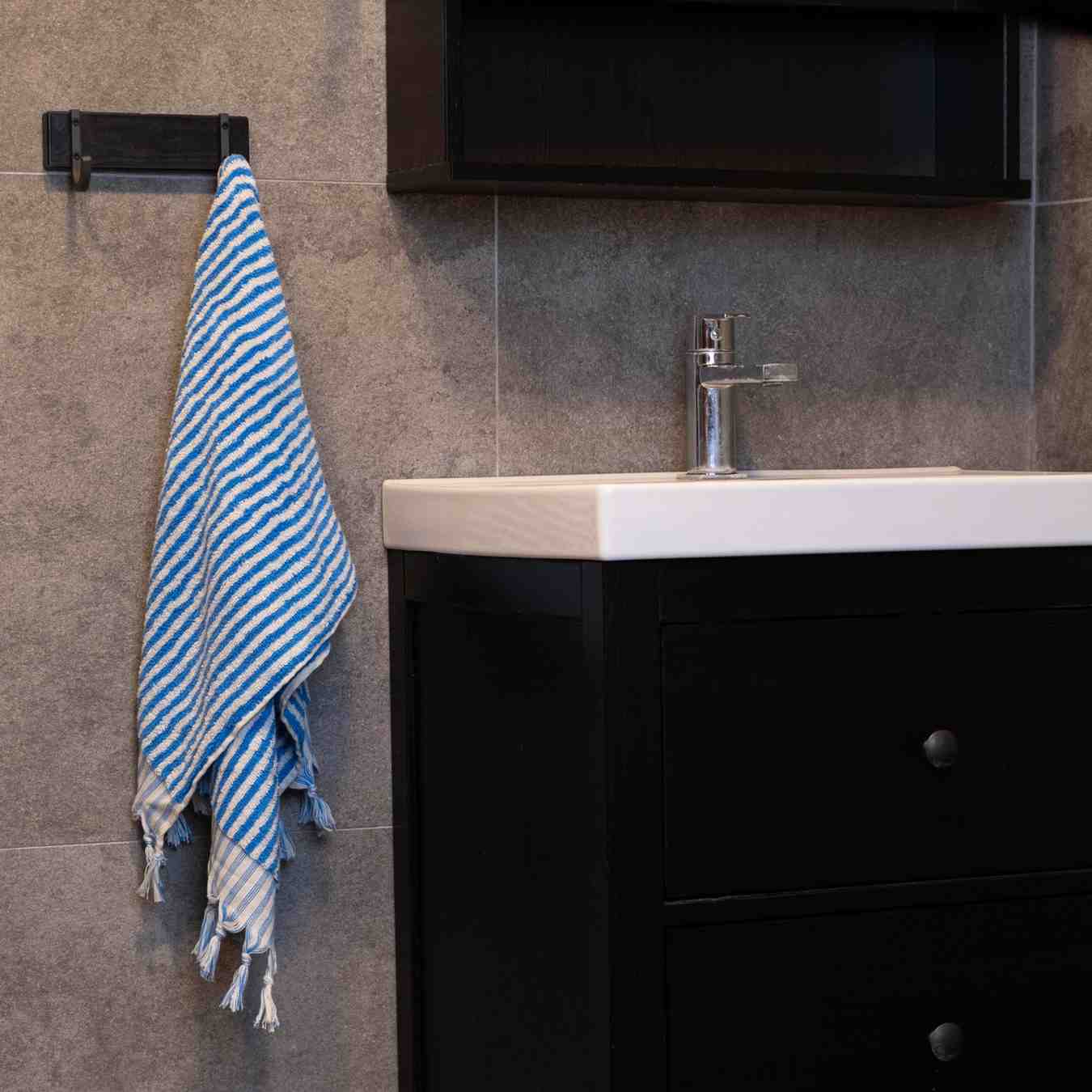 Blue striped hand towel hanging in modern bathroom beside black vanity sink.