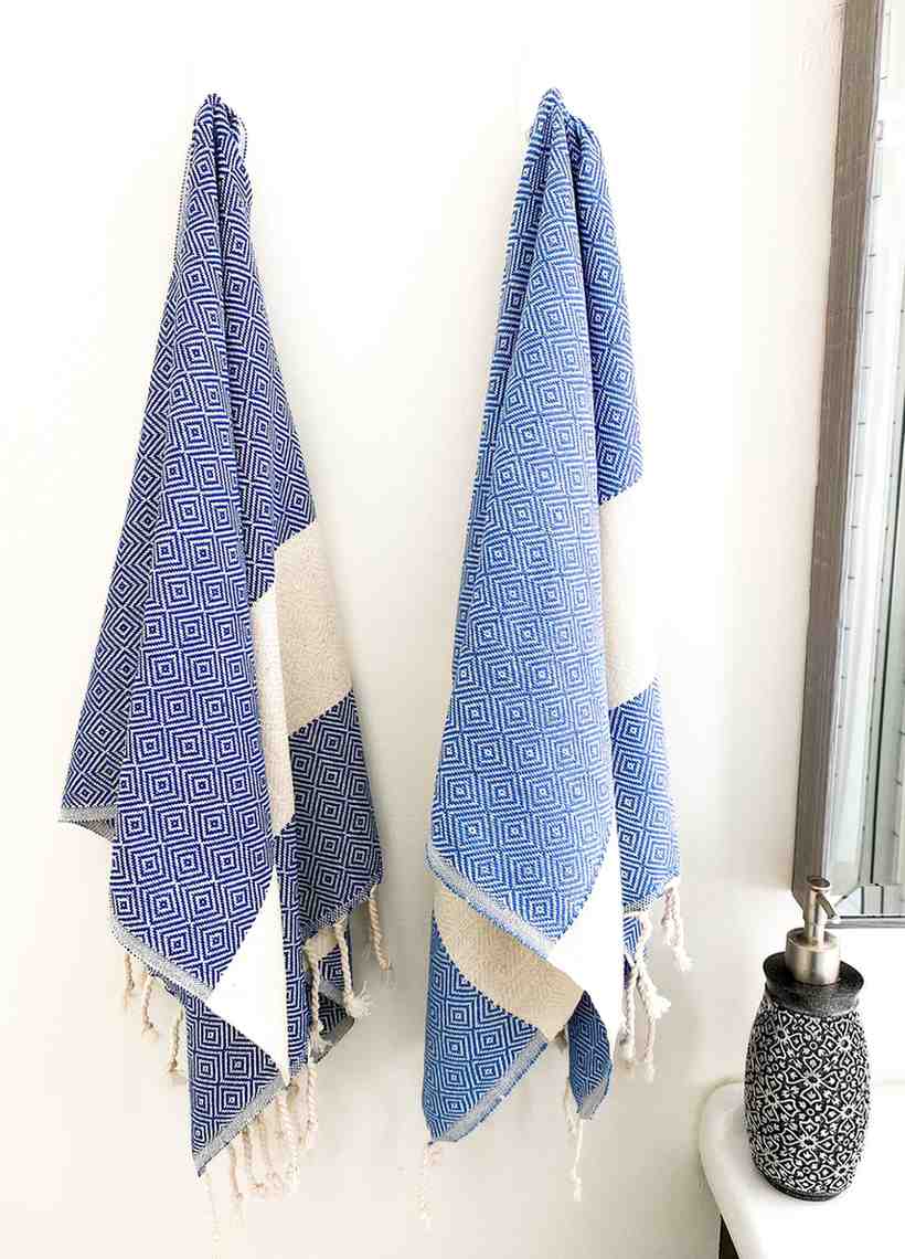 Blue diamond pattern hand towels with fringe hanging on white wall near soap dispenser