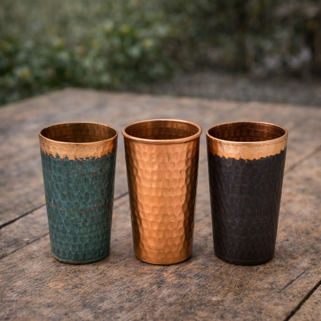 Three copper tumblers with different finishes on a wooden surface.