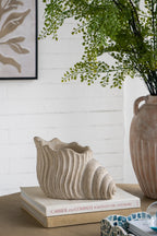 Decorative setting with a textured vase on books, a plant, and a framed picture on a white brick wall.