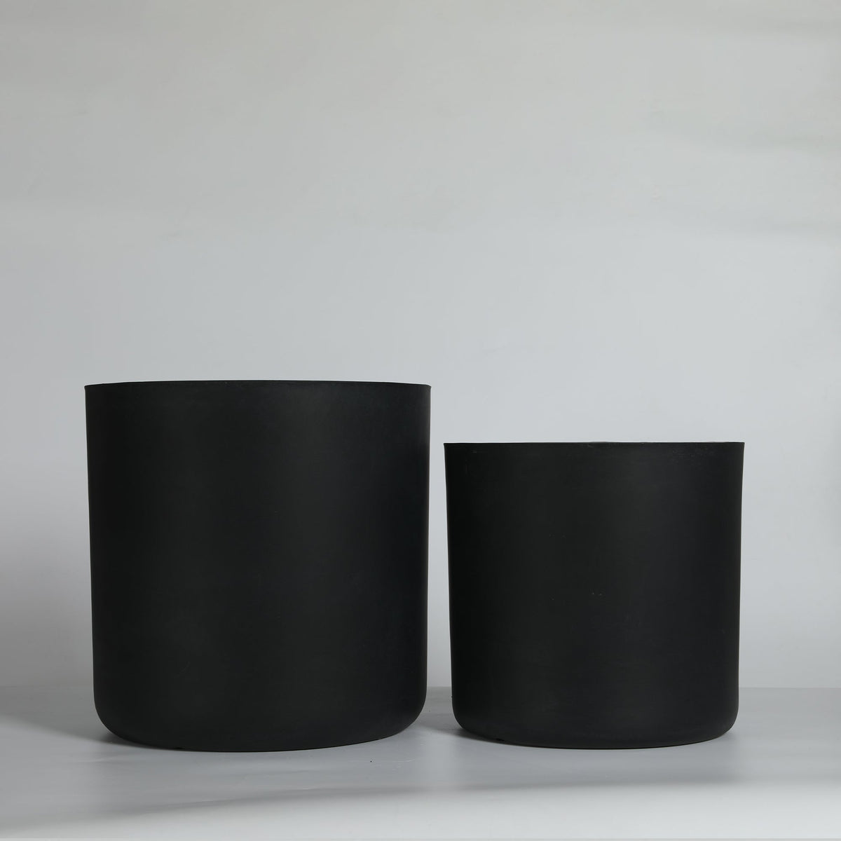 Two black cylindrical pots on a light gray background