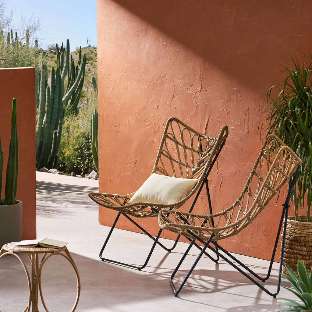 Wicker chair with a cushion on a patio with cacti and a terracotta wall.
