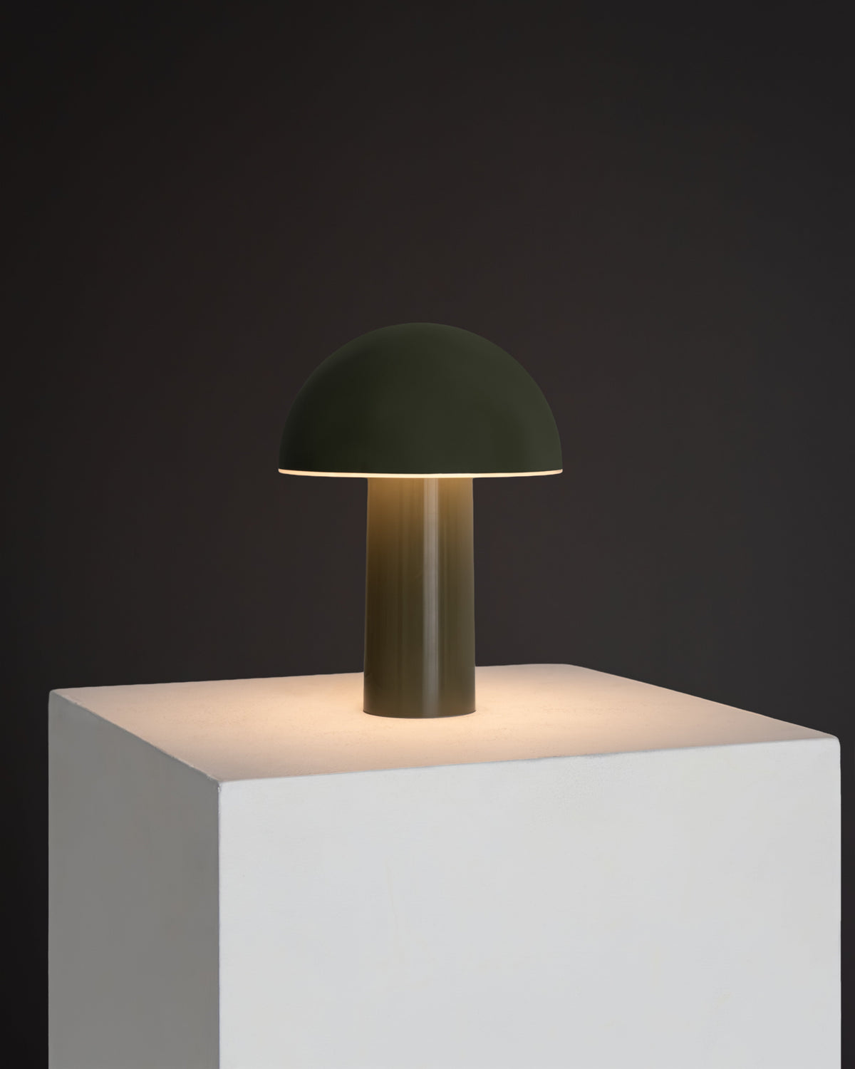 Modern table lamp with a green dome shade on a white pedestal against a dark background