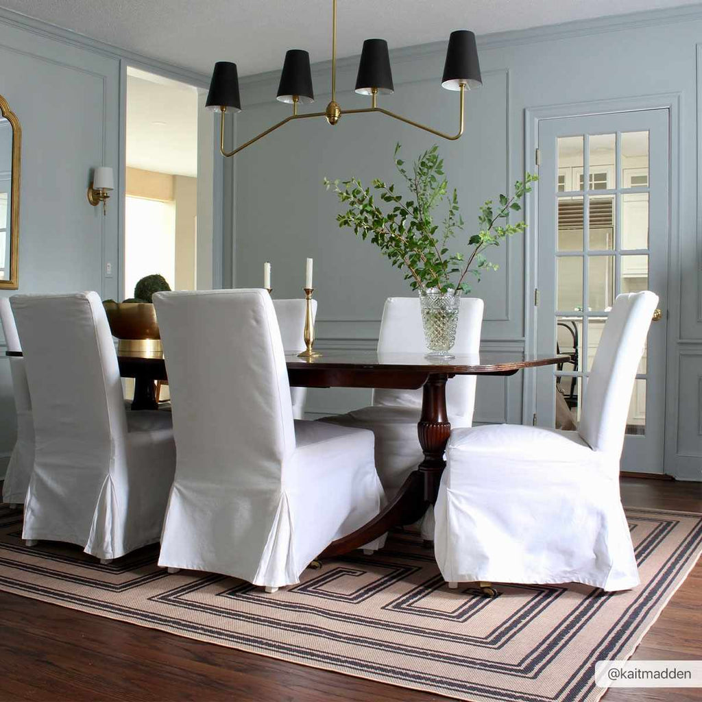 Dining room with a wooden table and white chairs on a striped rug.
