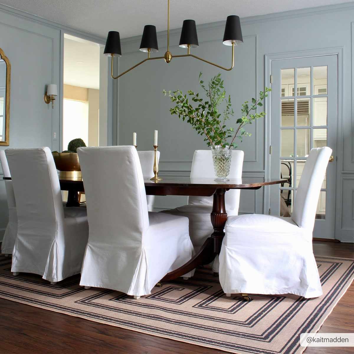 Dining room with a wooden table and white chairs on a striped rug.