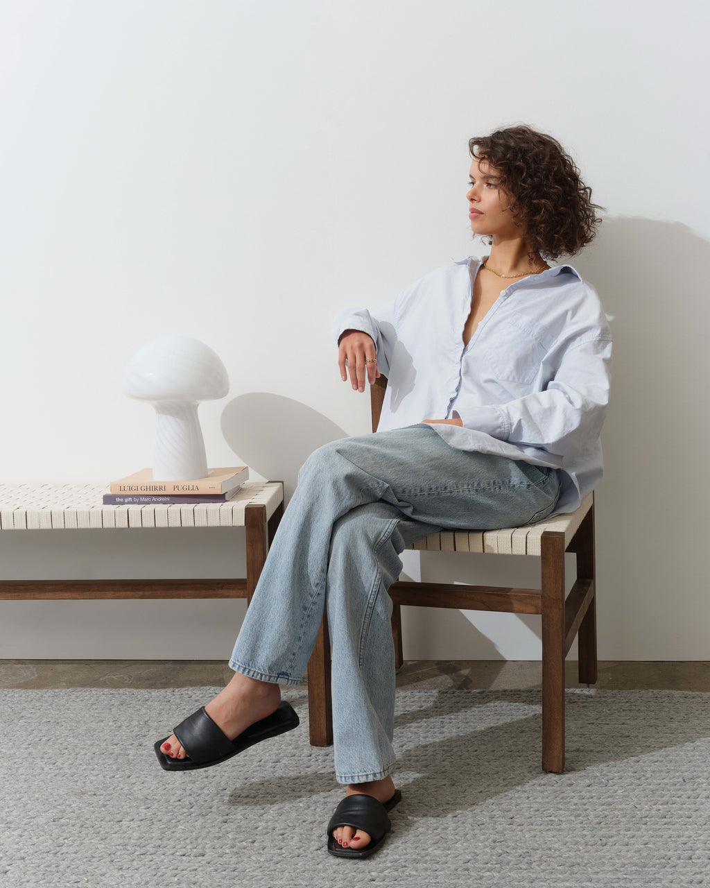Woman sitting on a chair in a minimalistic room with a white table lamp.