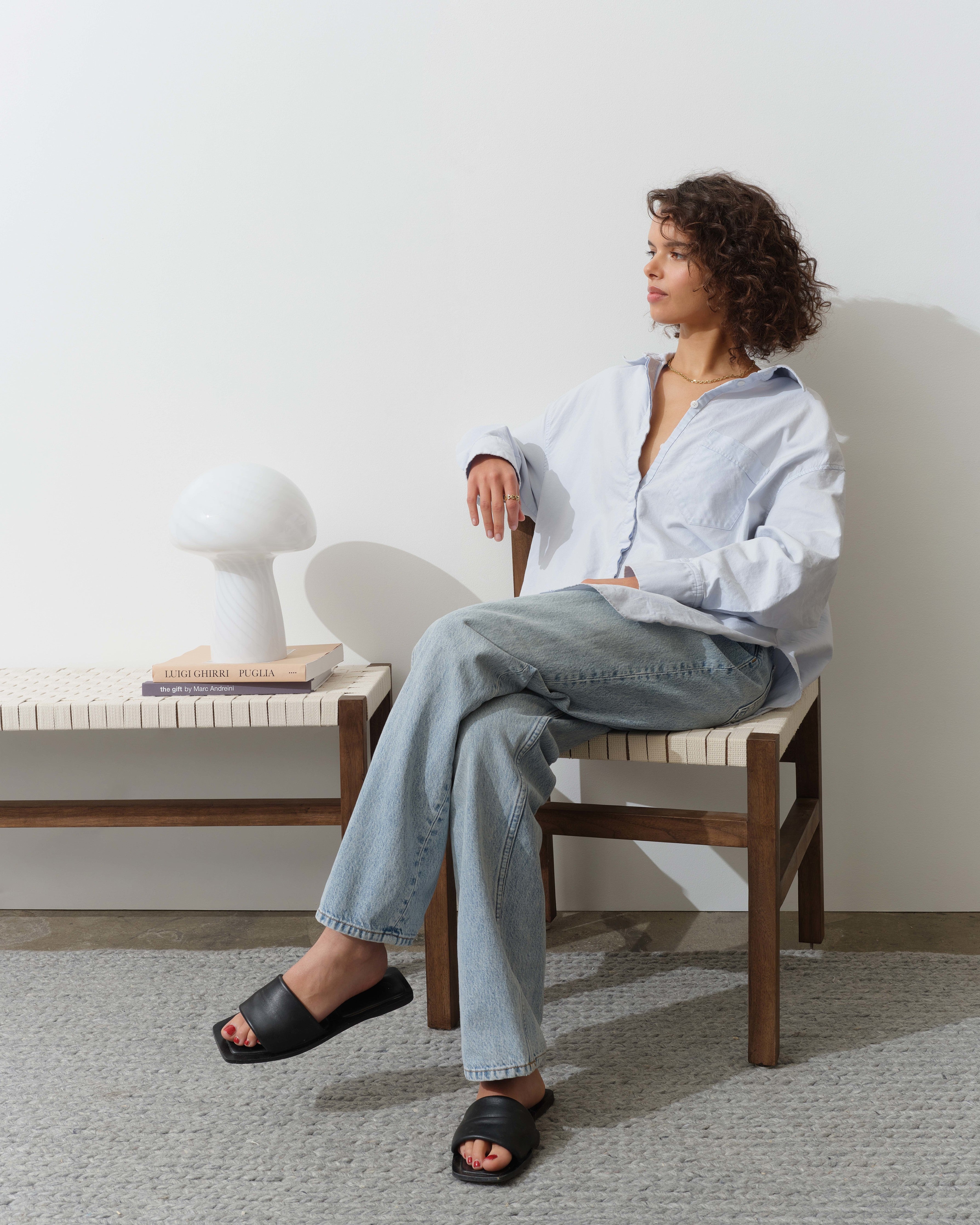 Woman sitting on a chair in a minimalistic room with a white table lamp.