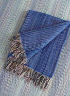Folded dark blue king size blanket with multicolor fringe on a woven surface