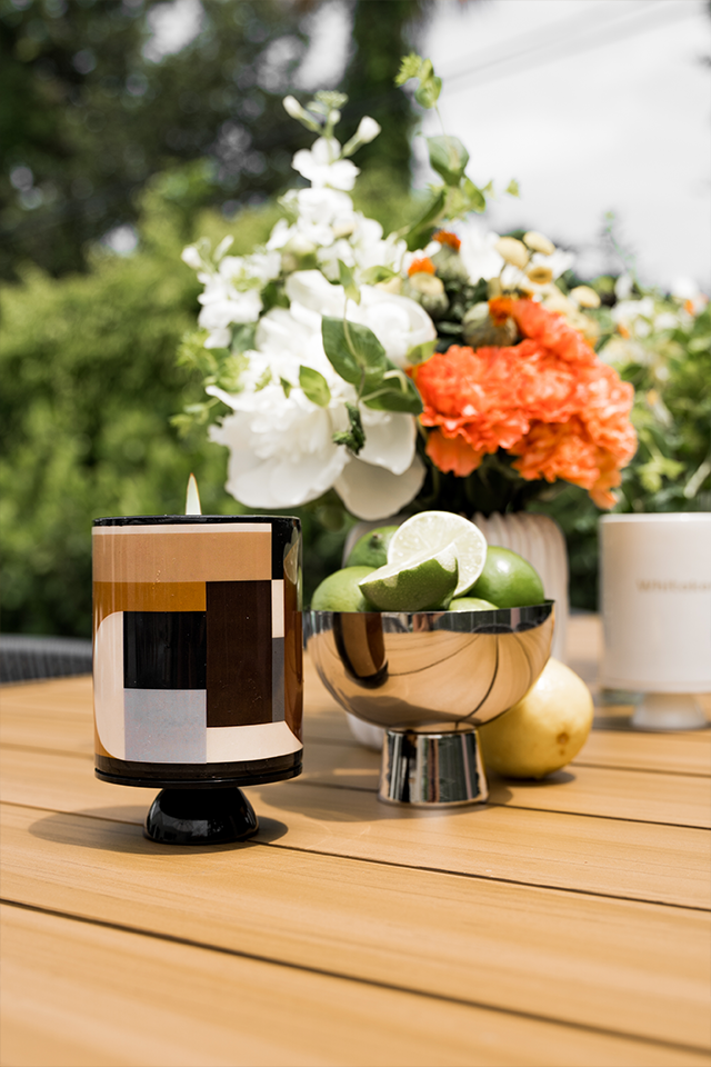 Decorative candle with geometric design on a wooden surface with flowers in the background
