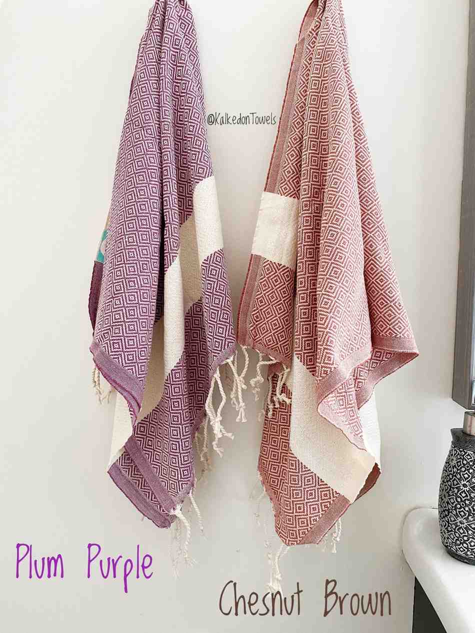 Eco-friendly Turkish tea guest towels in plum purple and chestnut brown with diamond pattern and fringe, hanging in a modern bathroom.