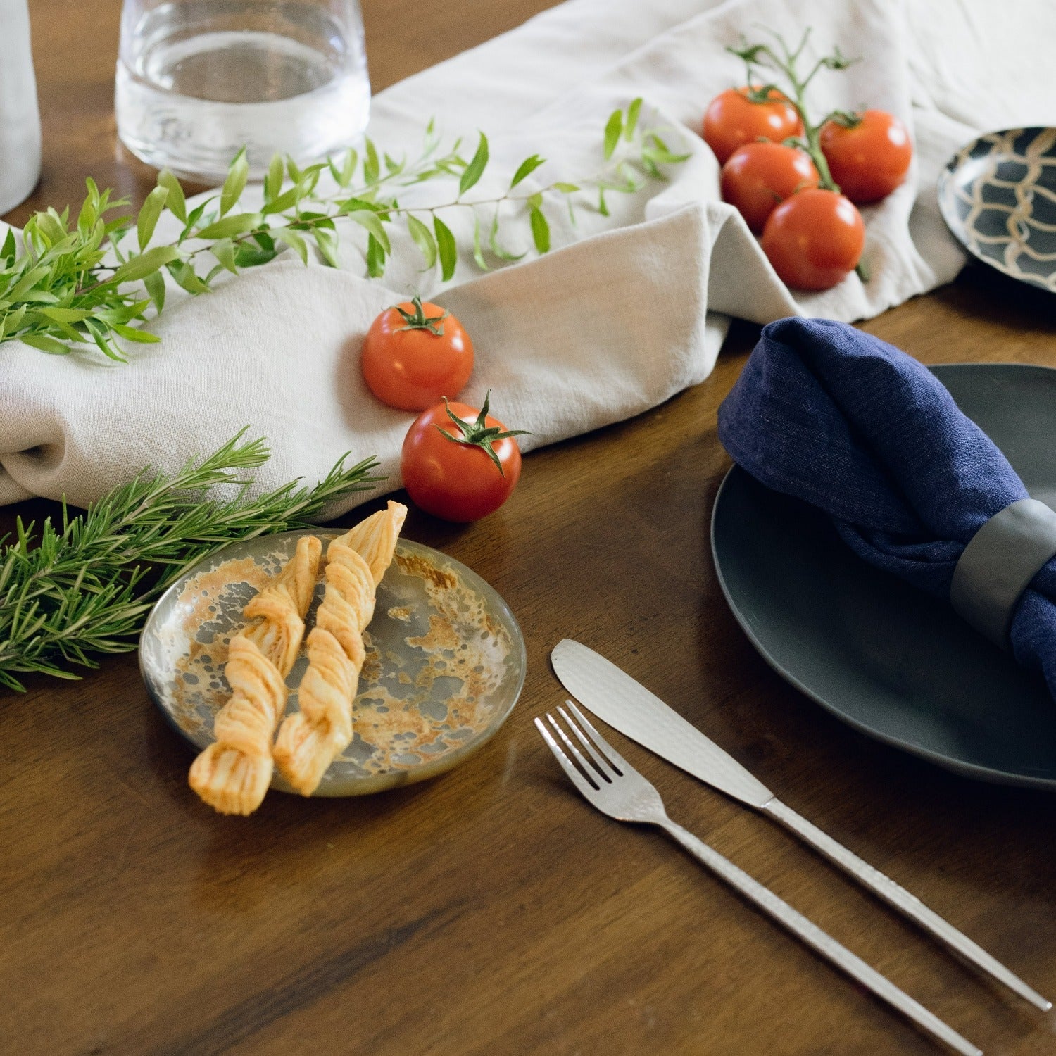 Table setting with pasta, tomatoes, and cutlery on a wooden surface