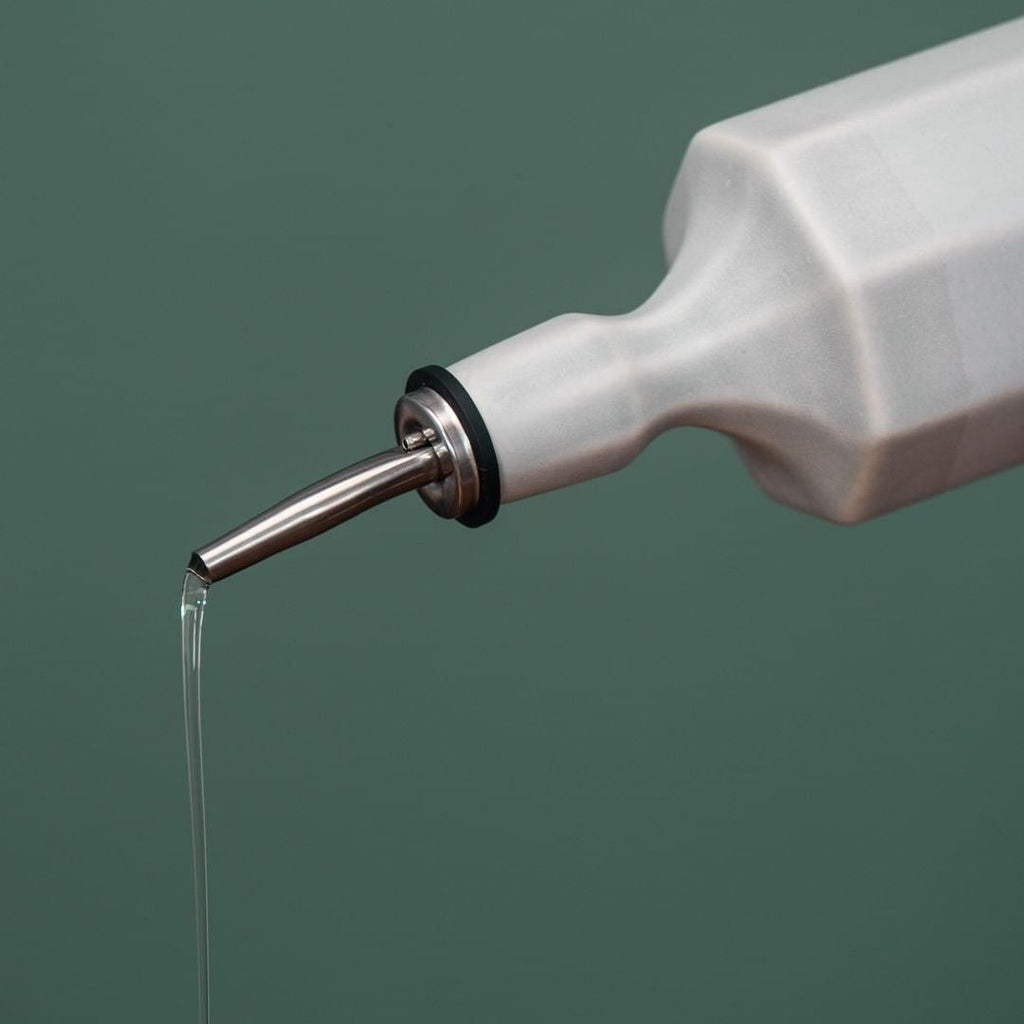 White bottle with a metal nozzle dispensing liquid on a green background