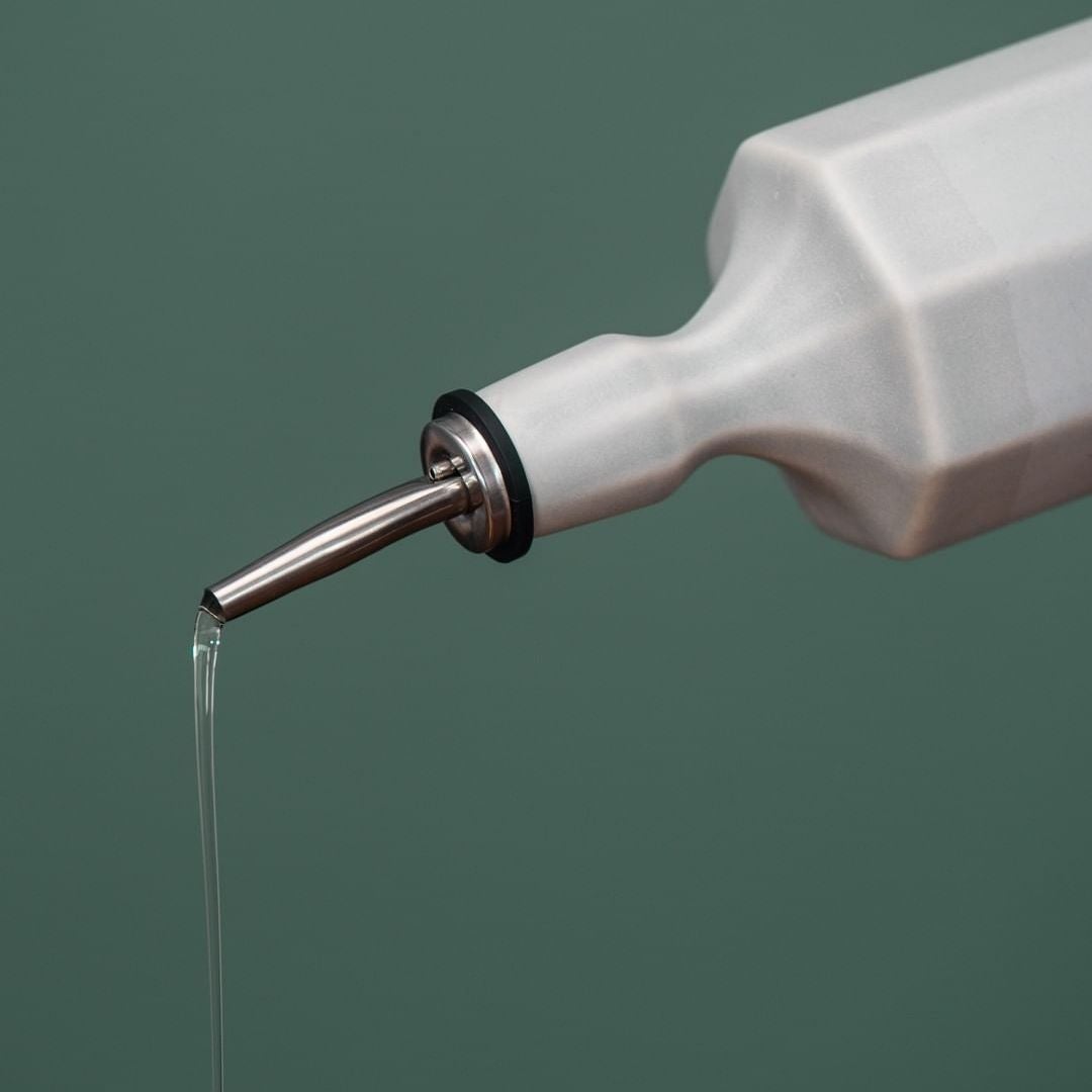 White bottle with a metal nozzle dispensing liquid on a green background