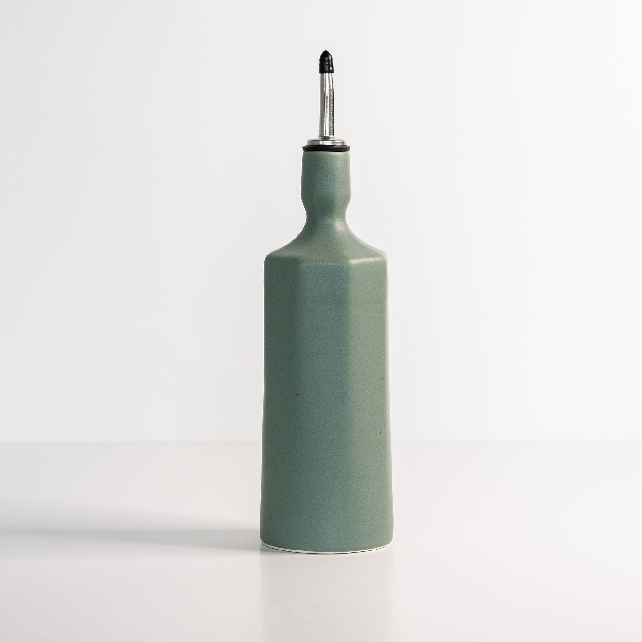 Green ceramic oil bottle with a black cap on a white background