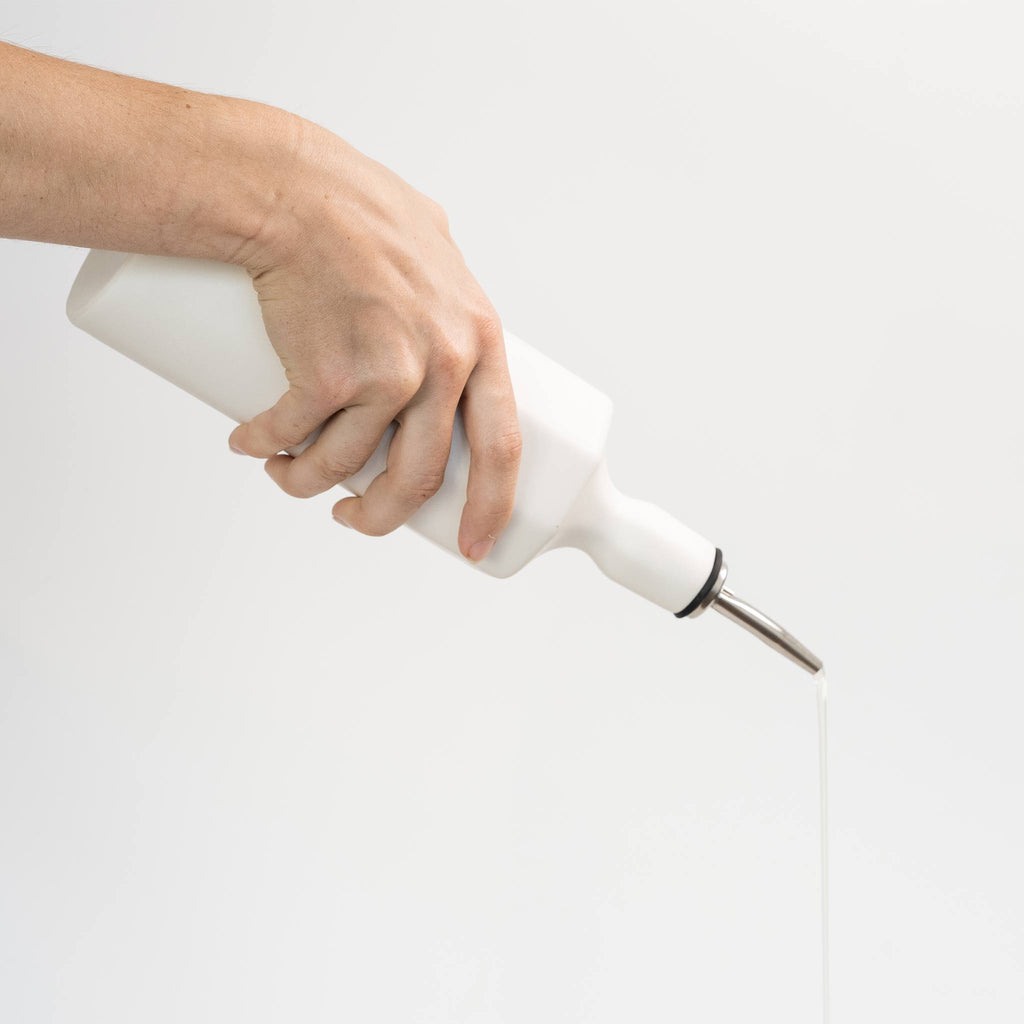 Hand holding a white handheld milk frother on a light gray background