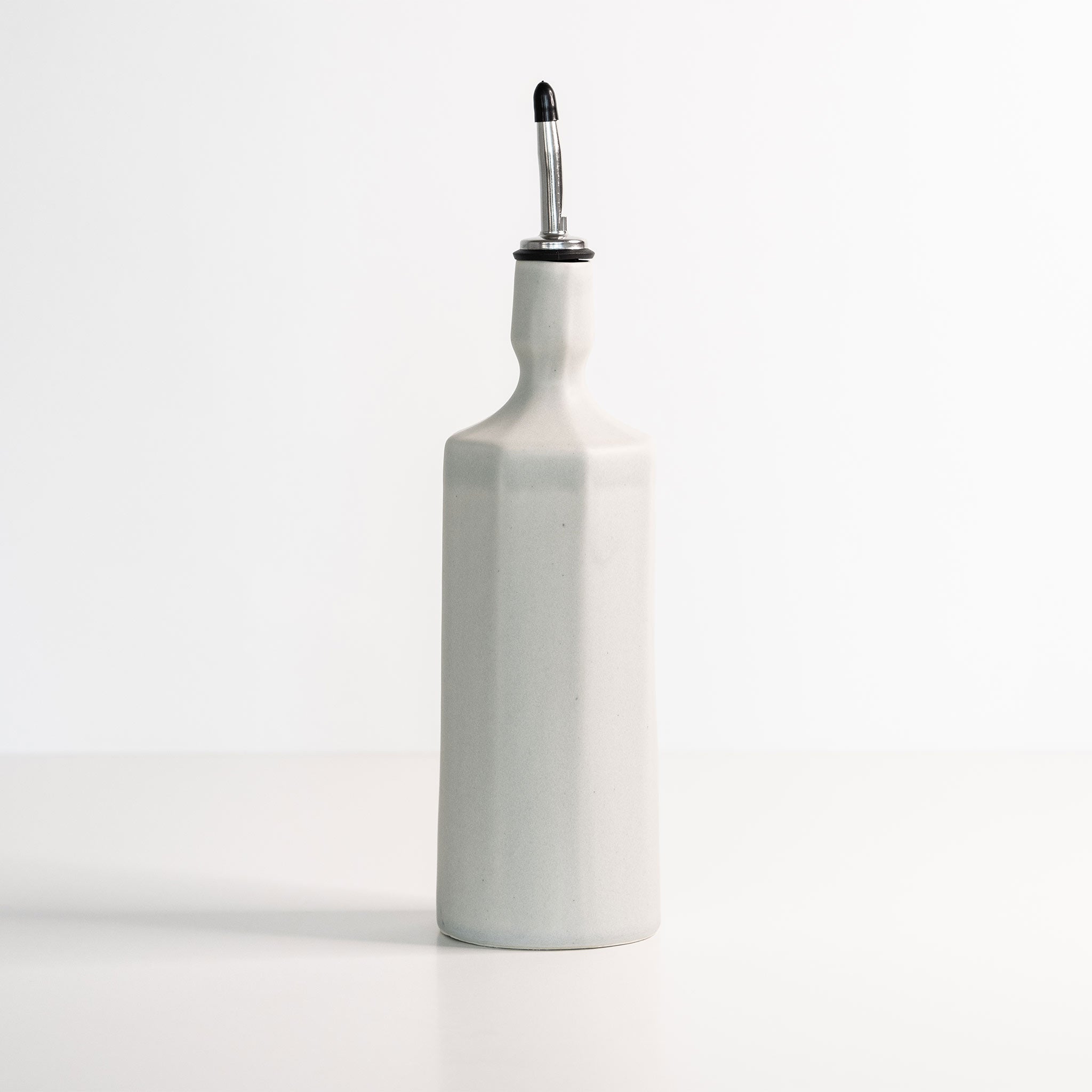 White ceramic olive oil bottle with a silver spout on a white background